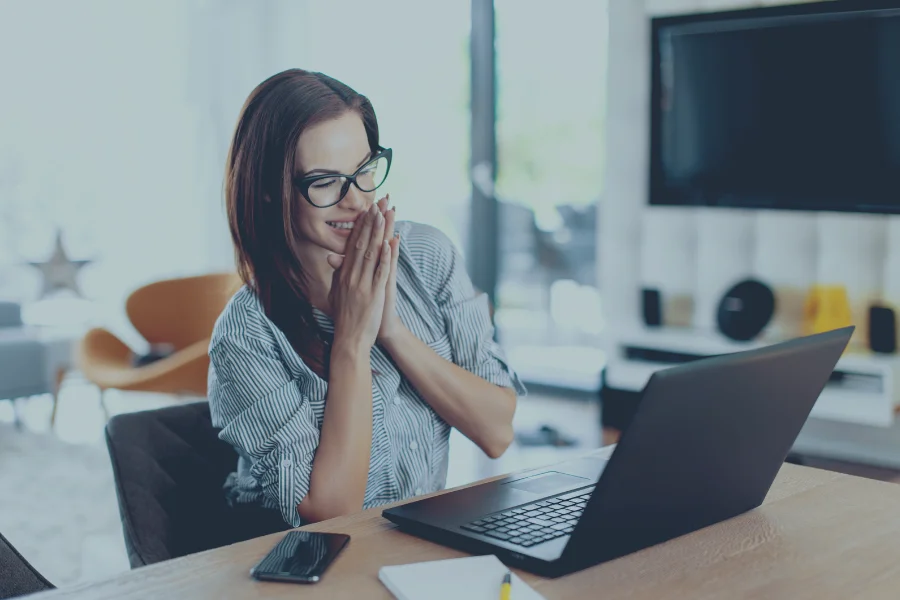 Smiling woman at her laptop celebrating the start of her Airbnb management business from a modern home office.