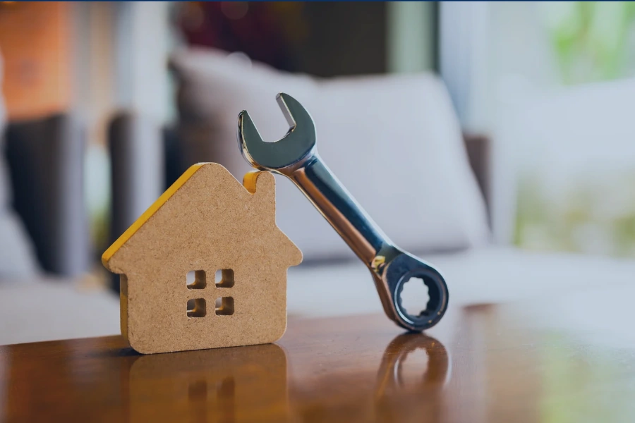 Wooden house model beside a wrench, representing preventive vacation rental maintenance.