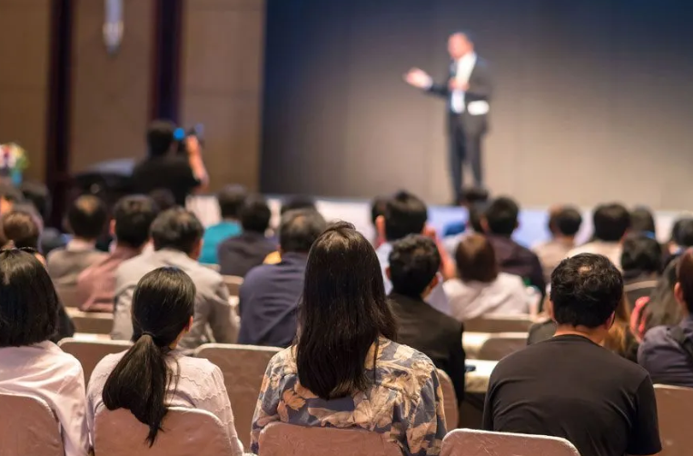 Audience seated in auditorium watching presenter on stage at vacation rental industry conference or event