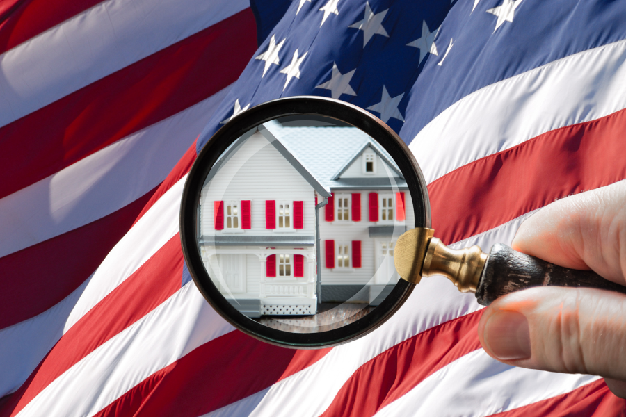 Hand holding magnifying glass over residential property illustration with American flag background