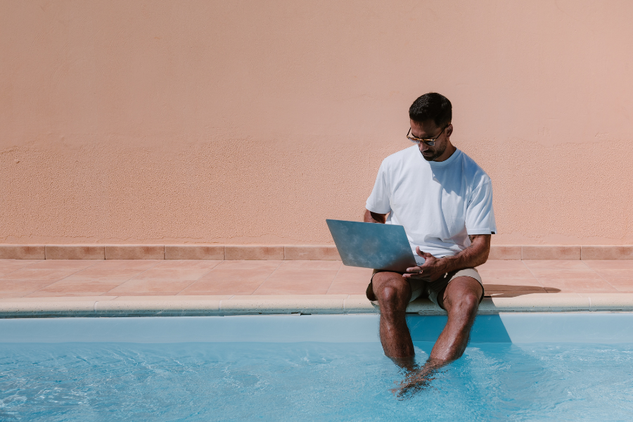 Man working on laptop by poolside while managing vacation rental operations
