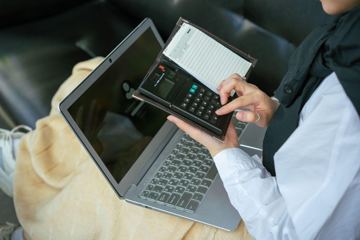 Property manager reconciling vacation rental trust account records with a calculator and laptop.
