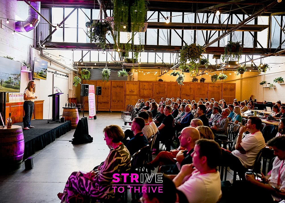 STRIVE 2026 conference attendees gathered in industrial warehouse venue with purple stage lighting and exposed beams