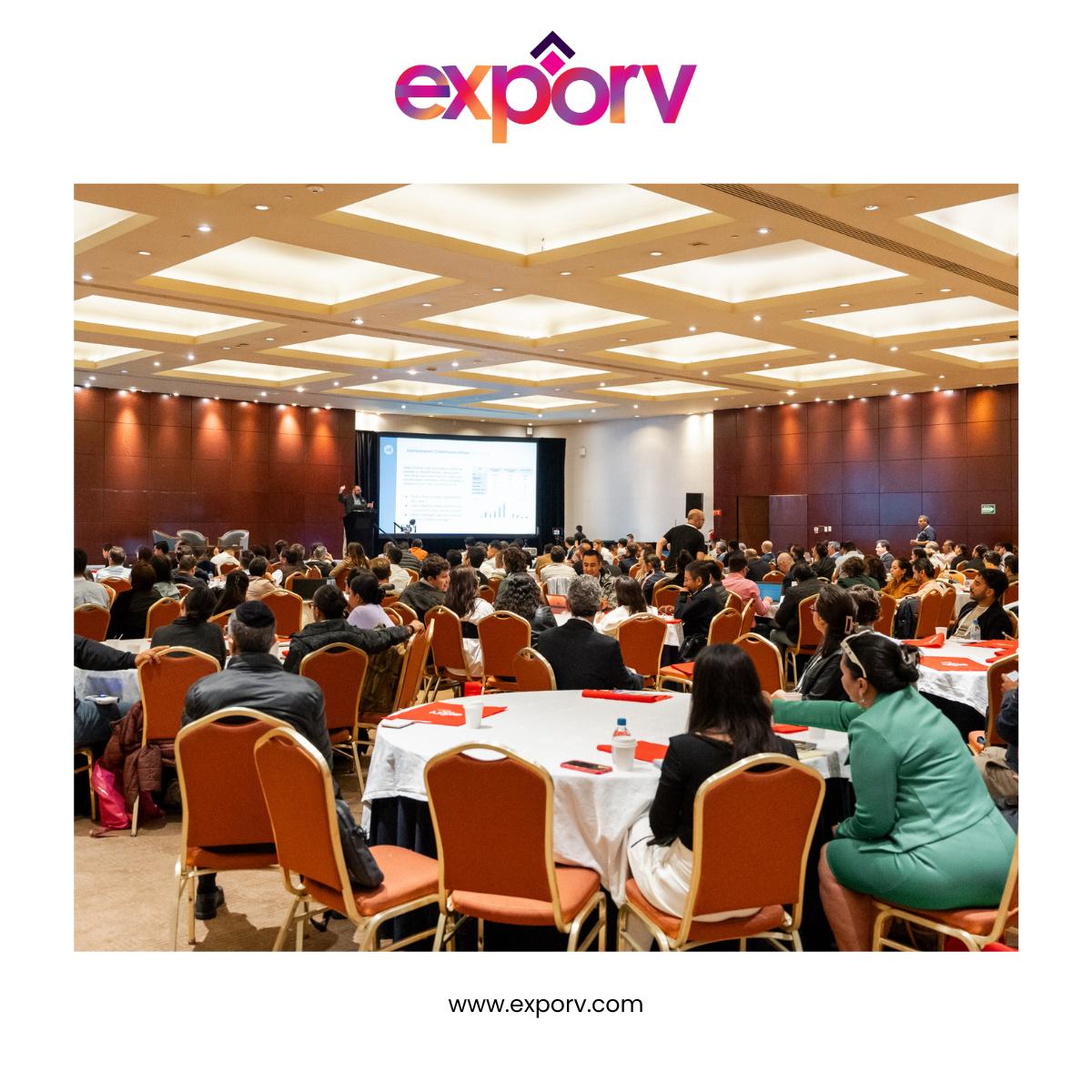 Large conference hall with attendees seated at round tables during ExpoRV National Conference, featuring projection screen and warm overhead lighting