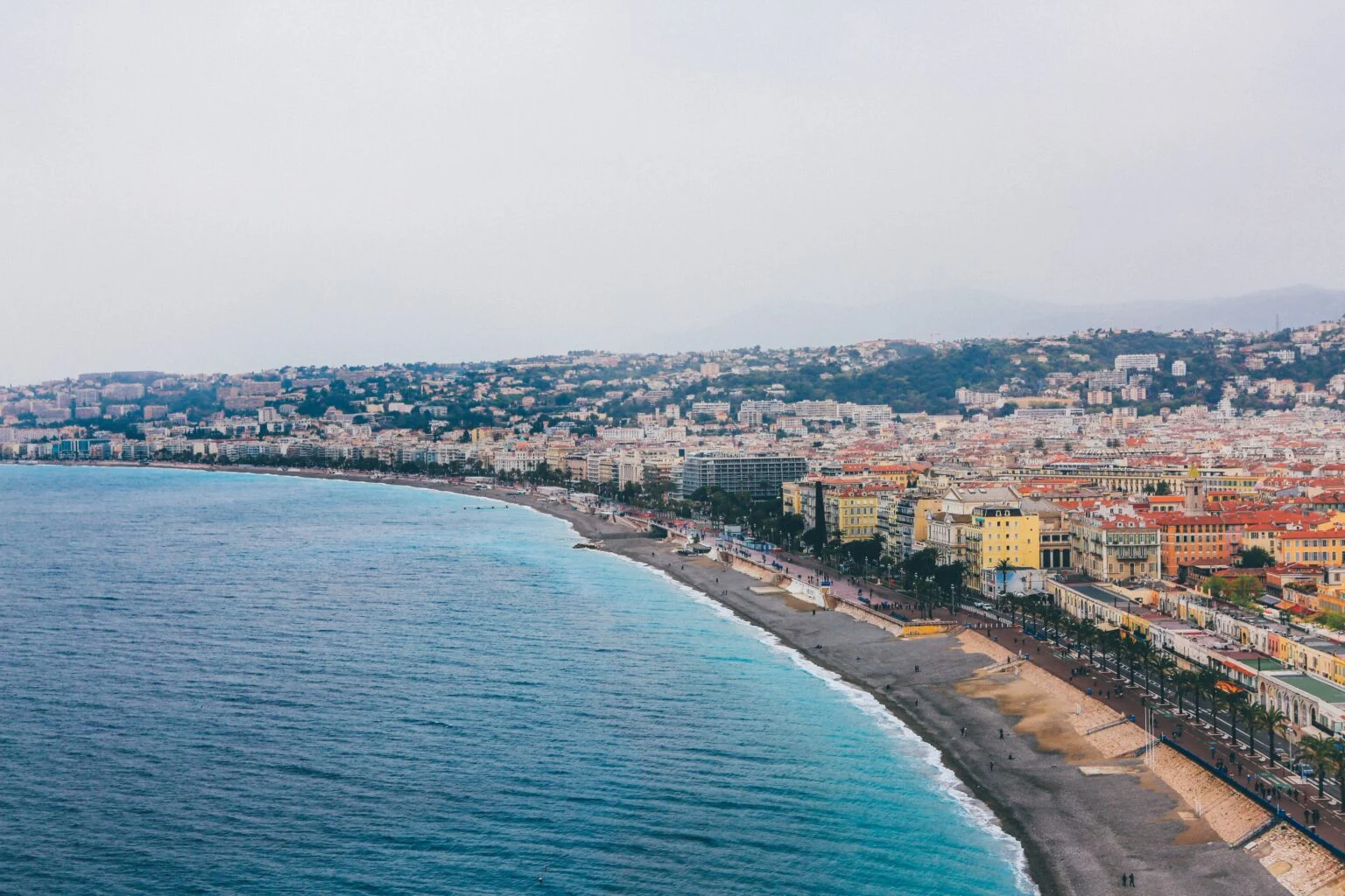 Coastal Mediterranean town with beach, turquoise sea and hillside buildings overlooking vacation rental destination.