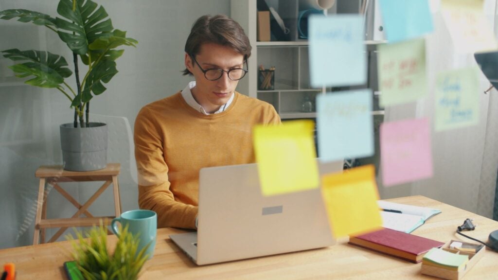 Property manager reviewing vacation rental bookings on laptop with sticky notes for task planning