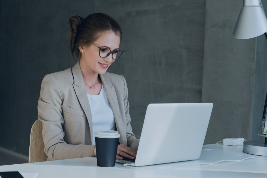 Anfitriã a trabalhar num computador portátil enquanto segura uma chávena de café num escritório moderno