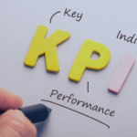 Letras amarillas que forman las siglas KPI con anotaciones explicativas: Key, Performance e Indicator, junto a un indicador rosa en superficie gris