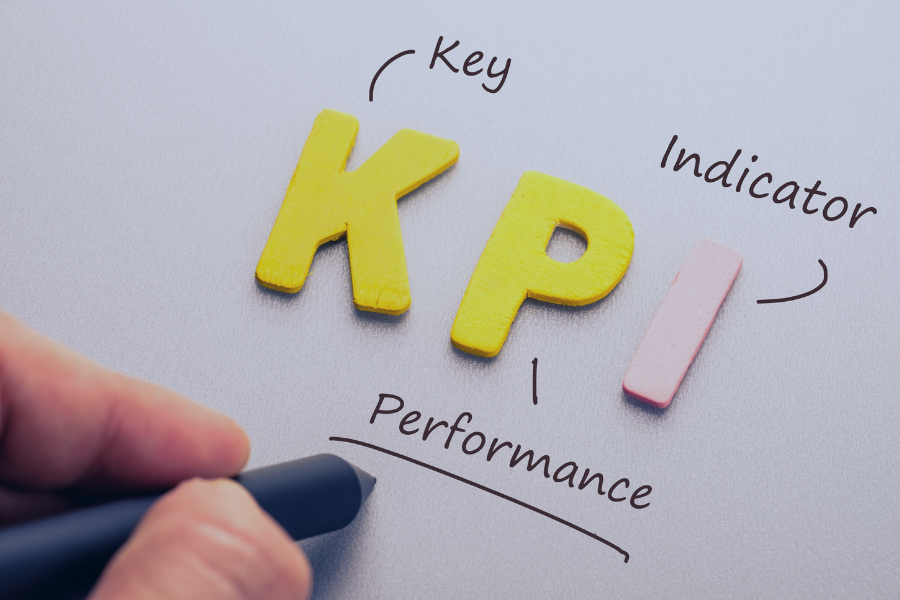 Letras amarillas que forman las siglas KPI con anotaciones explicativas: Key, Performance e Indicator, junto a un indicador rosa en superficie gris
