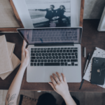 Property manager working at laptop surrounded by booking management tools, guest communication devices and framed holiday rental photographs