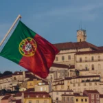 Portuguese flag flying above historic Lisbon buildings with terracotta roofs and a clock tower