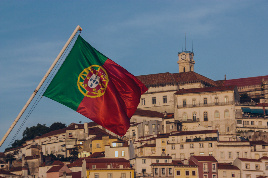 Portuguese flag flying above historic Lisbon buildings with terracotta roofs and a clock tower