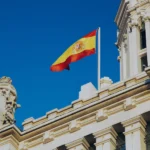Spanish flag flying above ornate white stone building facade against clear blue sky