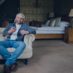 Host reviewing guest messages on mobile device while relaxing in bedroom suite