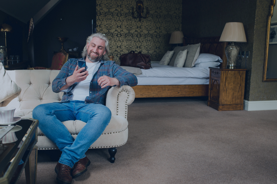 Host reviewing guest messages on mobile device while relaxing in bedroom suite