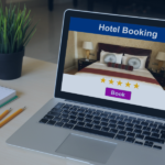 Laptop displaying hotel booking website with four-star rated bedroom and purple Book button, on desk with notepad and pencils