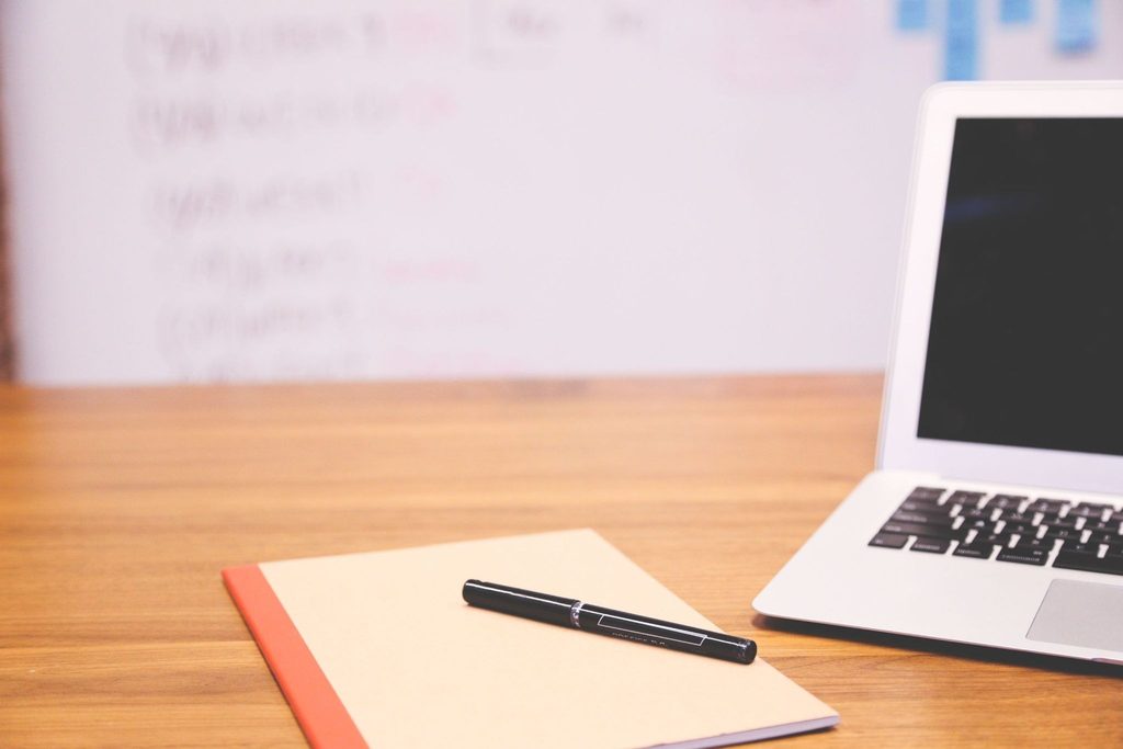 Notebook with black pen and laptop on wooden desk in office setting