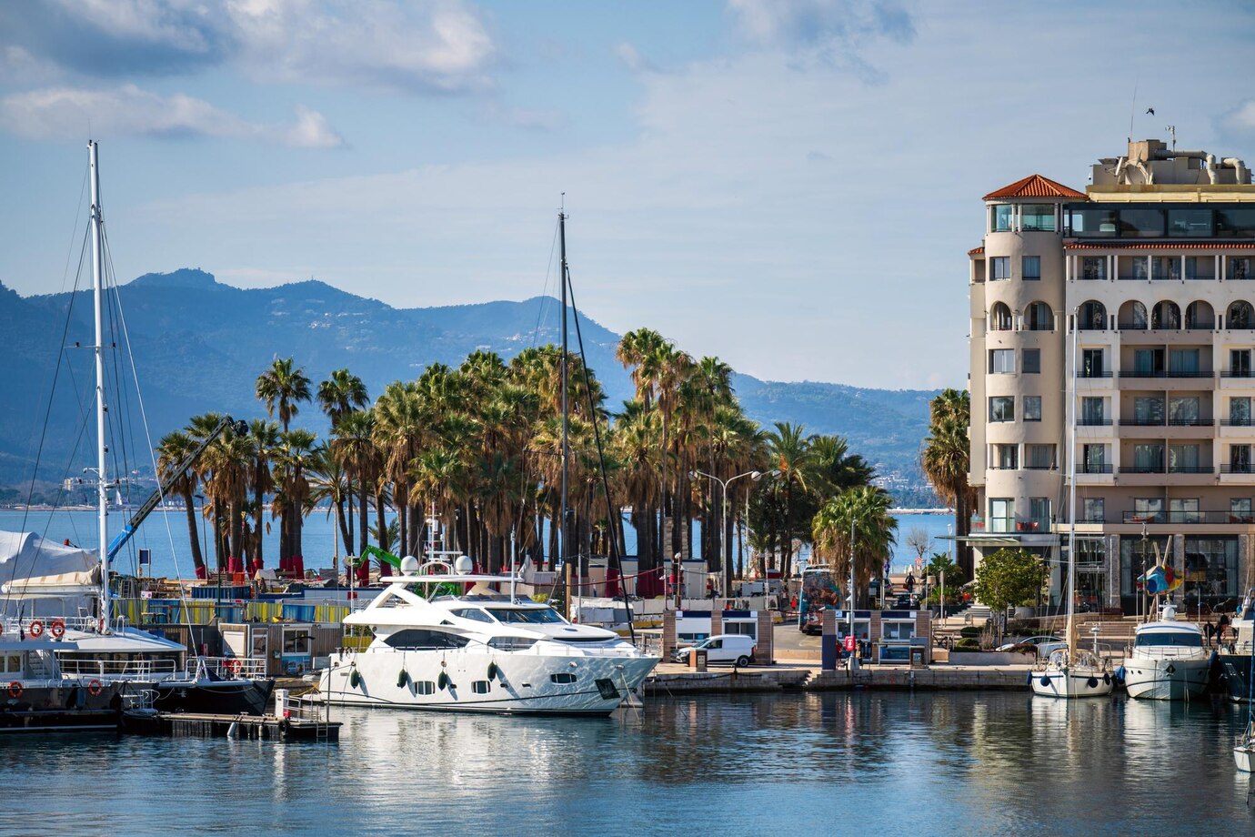 Waterfront marina in Cannes with moored yachts, palm trees and Mediterranean architecture beneath mountains
